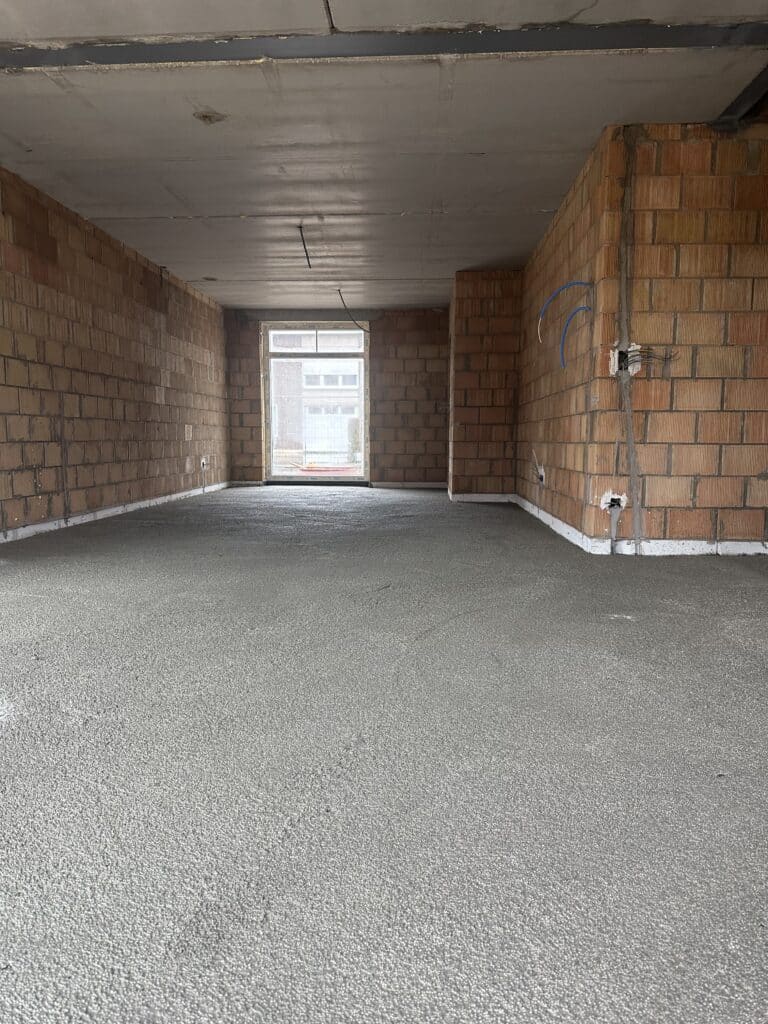 Chape finie dans un espace de construction neuve avec des murs en briques et des conduits électriques apparents – réalisation de chape